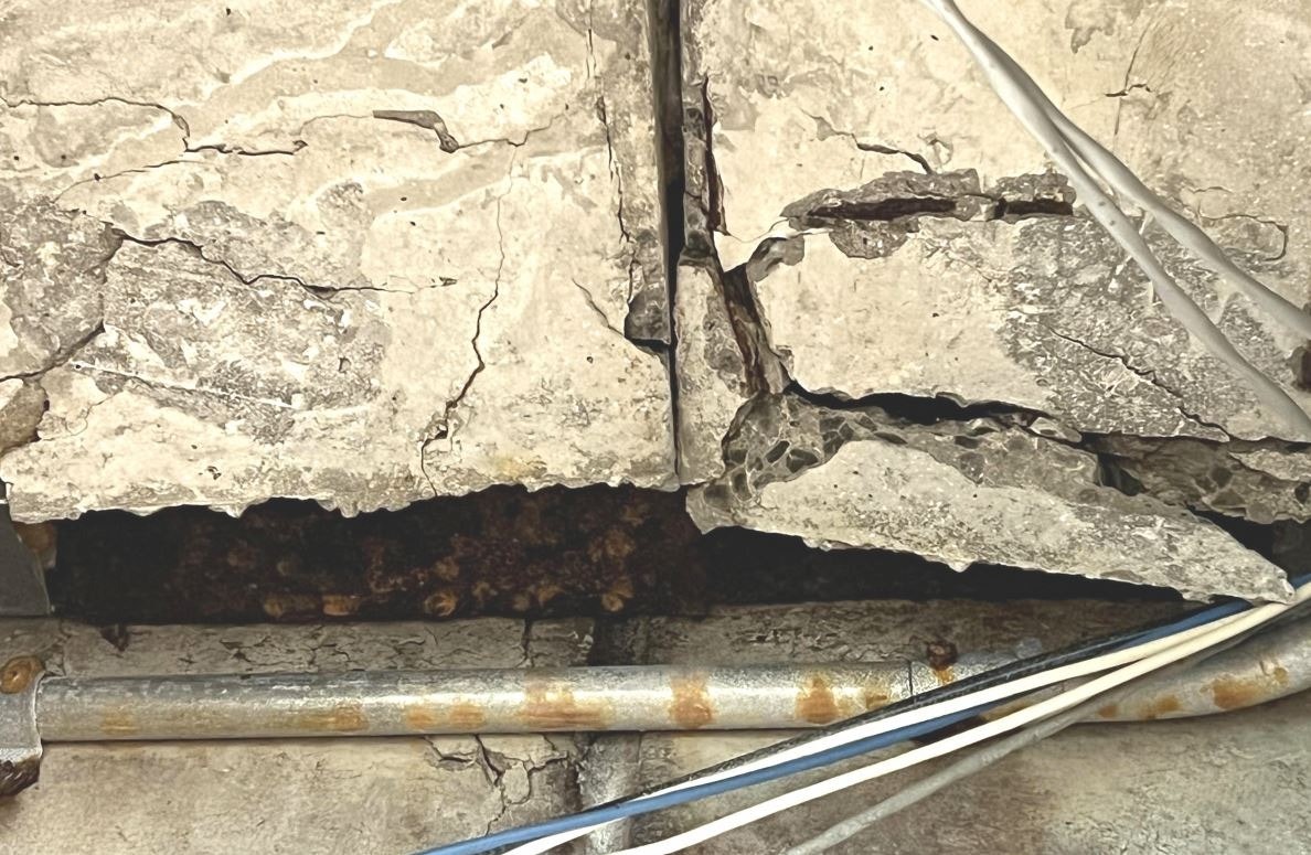 Cracked concrete with exposed rebar and electrical wires.