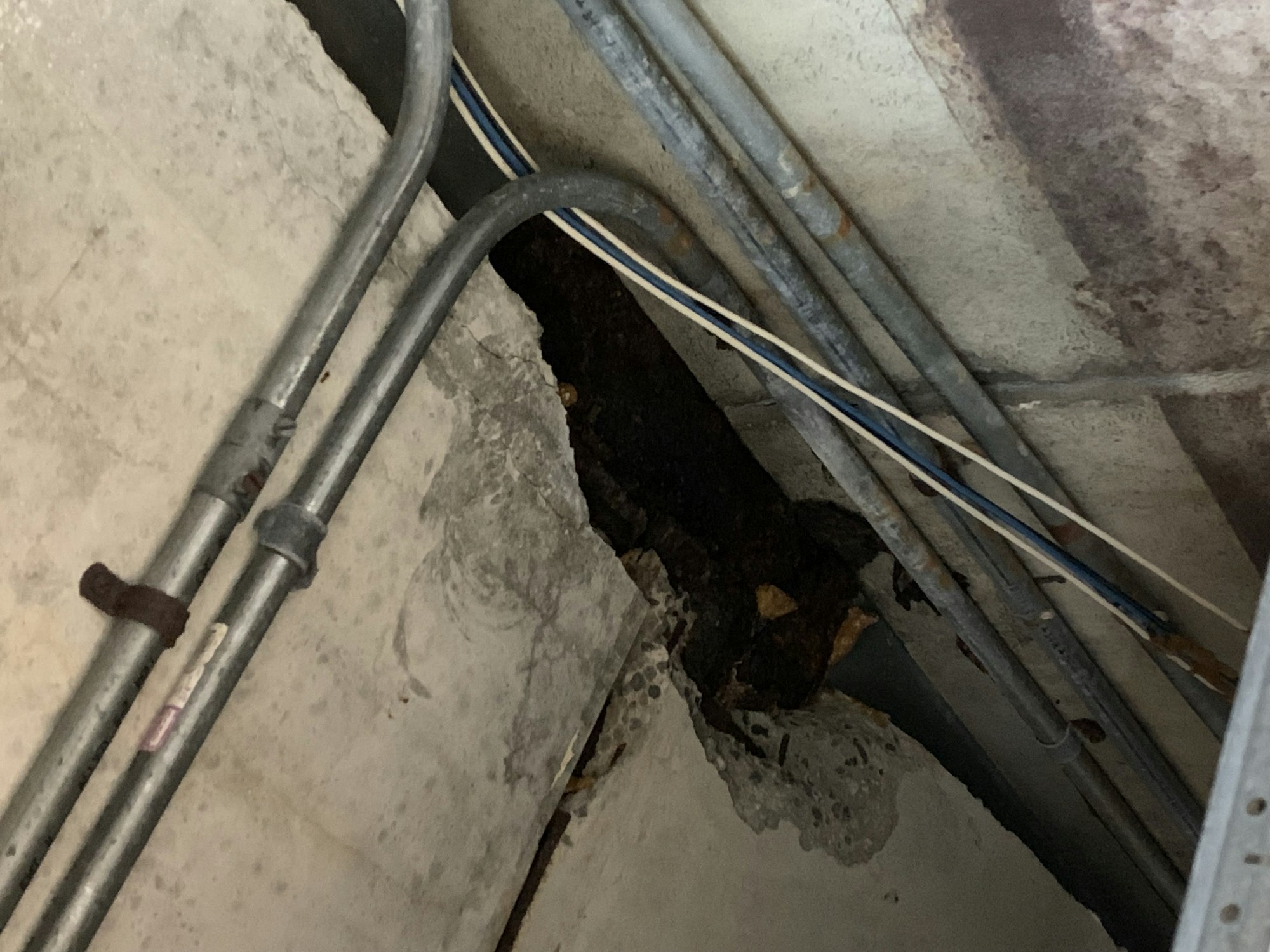 Pipes and cables on a concrete wall with a dark area, possibly damage.