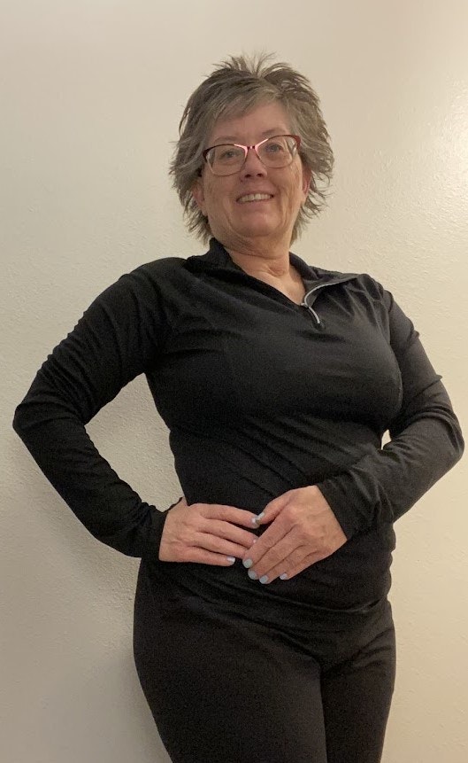 A person wearing glasses and dressed in black poses confidently against a light-colored wall.