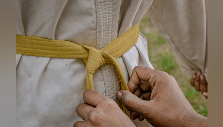 Close-up of hands tying a yellow martial arts belt around a white uniform.