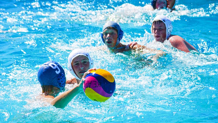 A water polo match in progress with players in caps aiming for the ball.