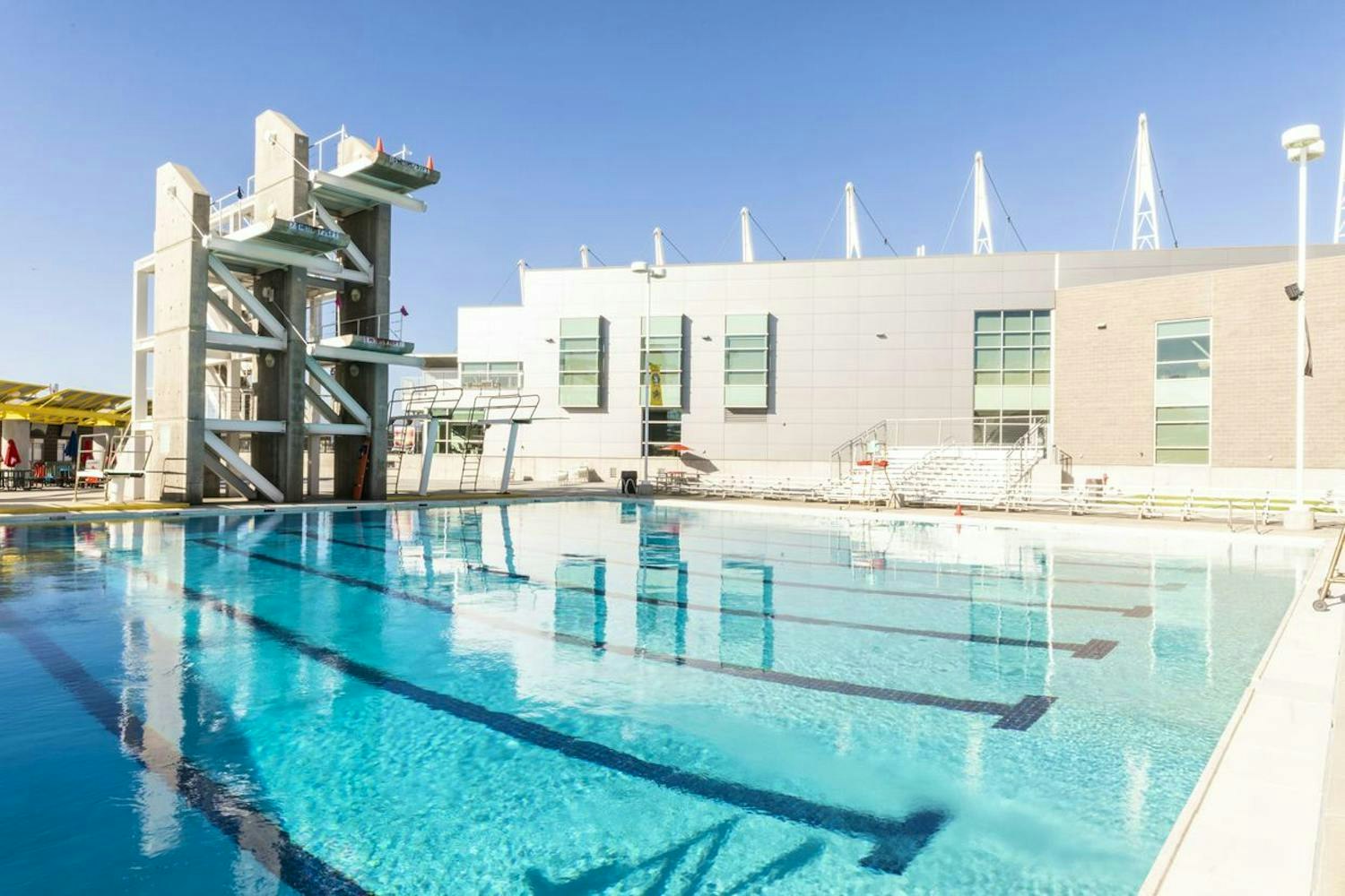 Outdoor swimming pool with diving platforms and a clear blue sky.