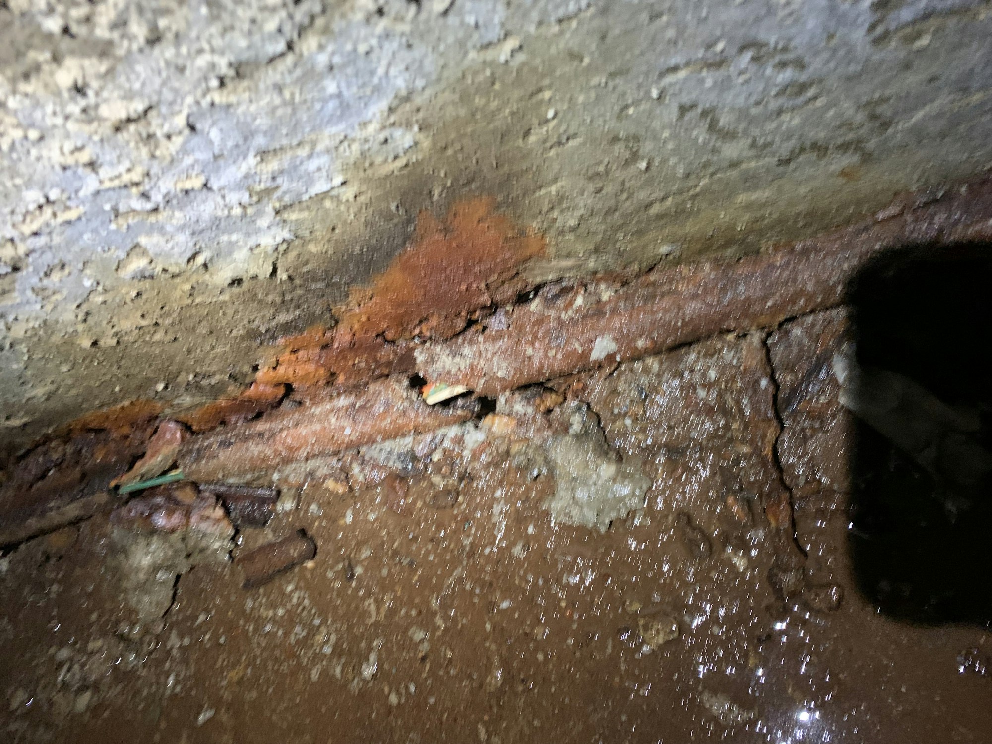 Rusted metal and crumbling concrete with some water damage, under dim light.