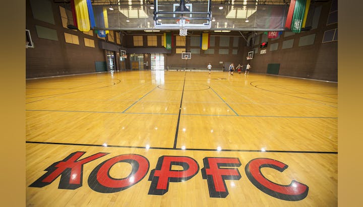 Indoor basketball court with players in the background and a big logo on the wooden floor.