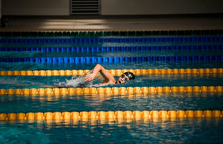 A swimmer in goggles and cap doing backstroke in a pool with lane markers.