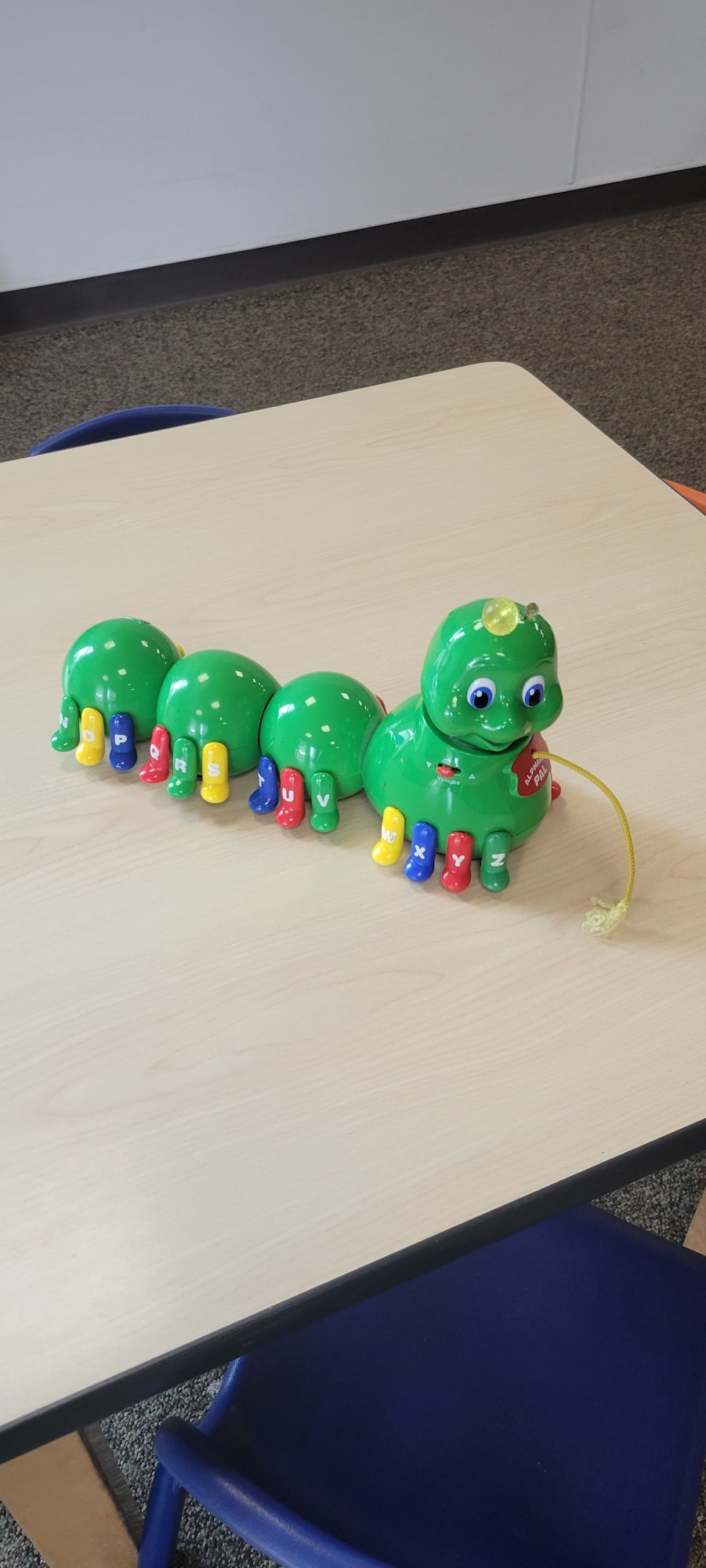 A colorful caterpillar toy with letters and numbers on a wooden table, beside a blue chair.