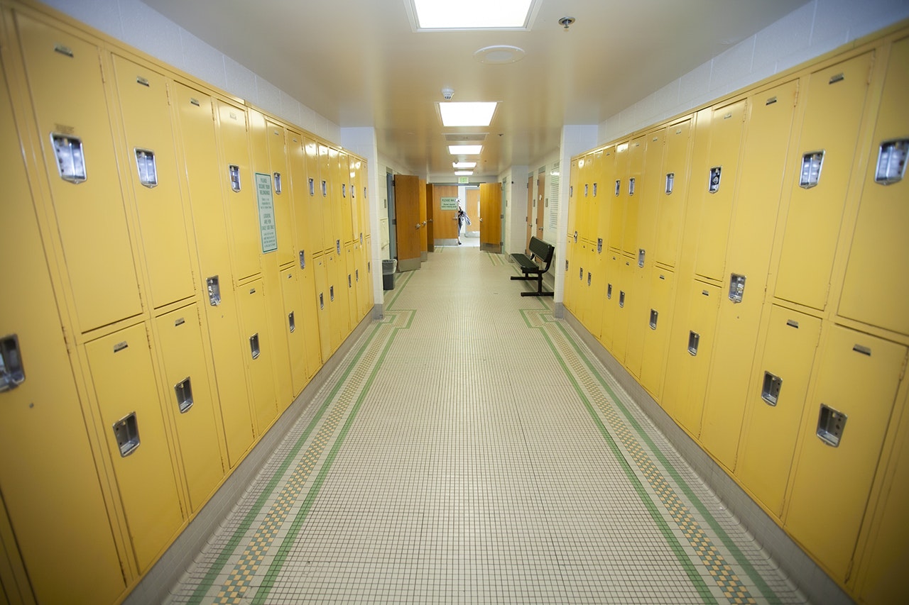A corridor with rows of yellow lockers and a bench, likely in a school or gym.