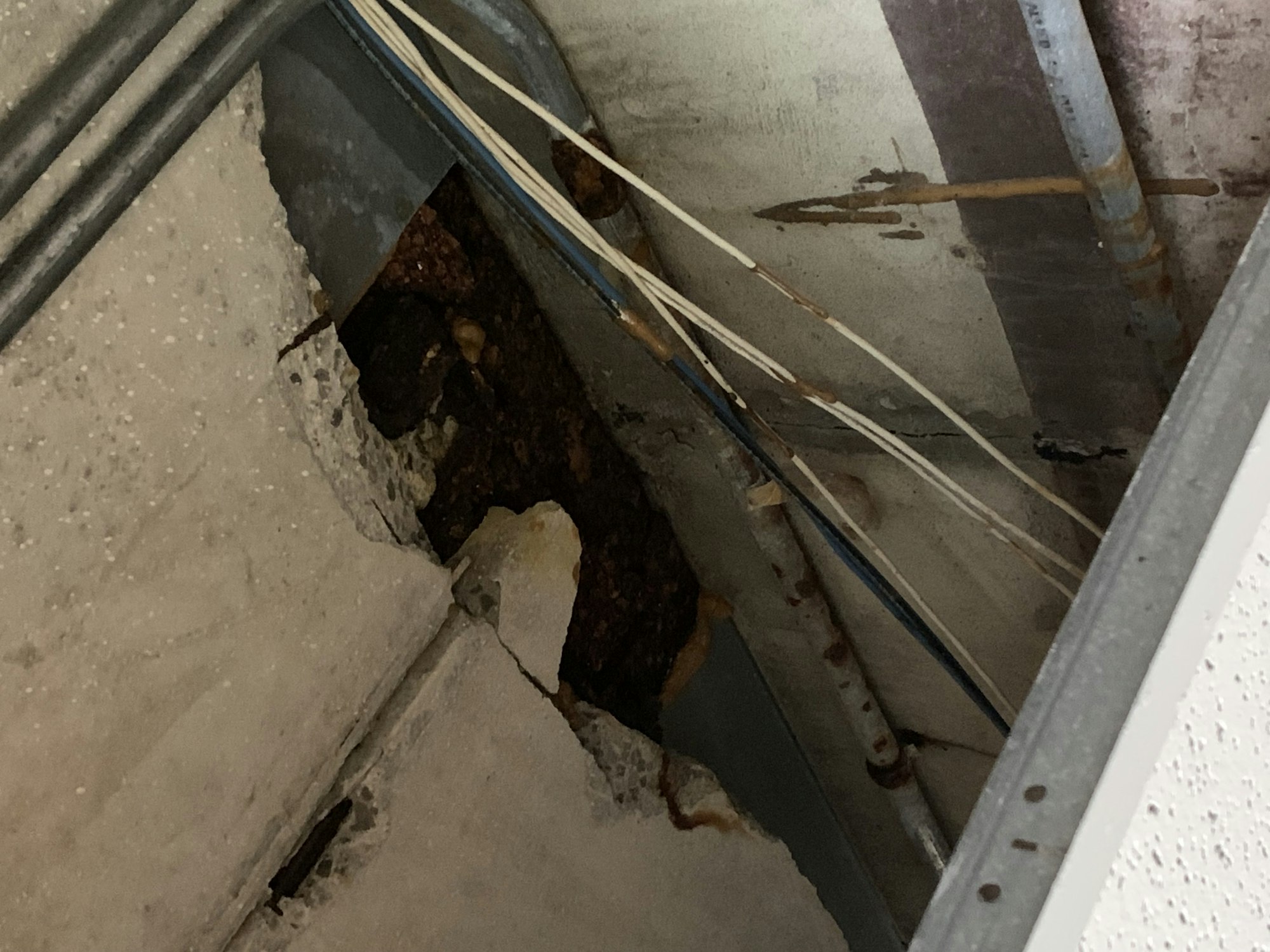 A damaged ceiling with exposed wires and pipes, showing some concrete debris.