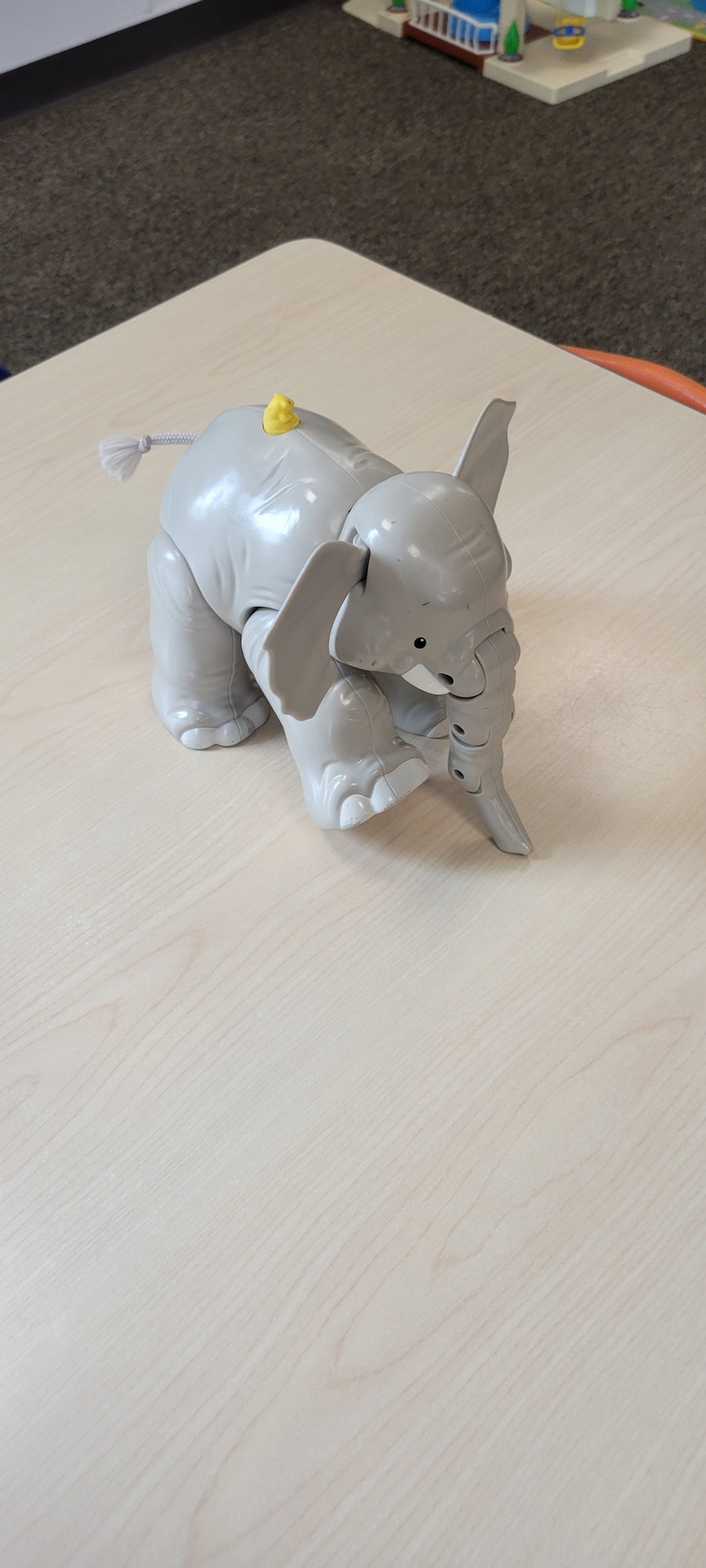 A grey ceramic figurine of two elephants, one on top of the other, with a yellow detail on a wood surface.