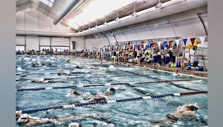 Indoor swimming pool with swimmers competing and spectators watching from the side.