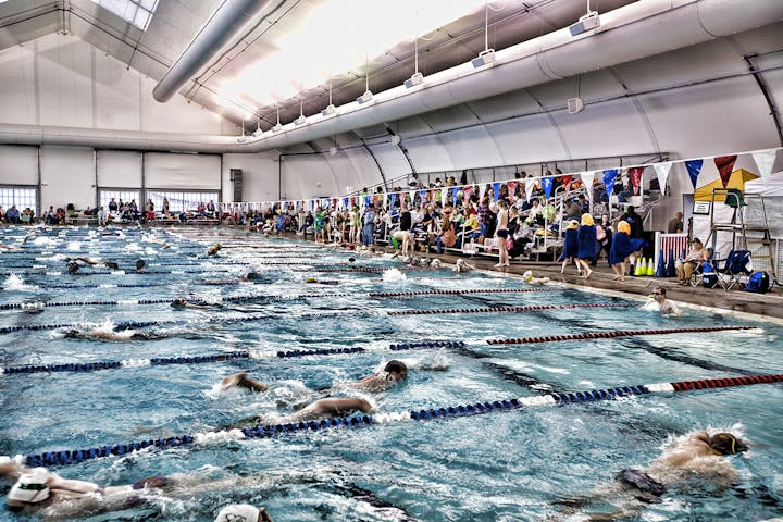 Indoor swimming pool with swimmers competing and spectators watching from the side.