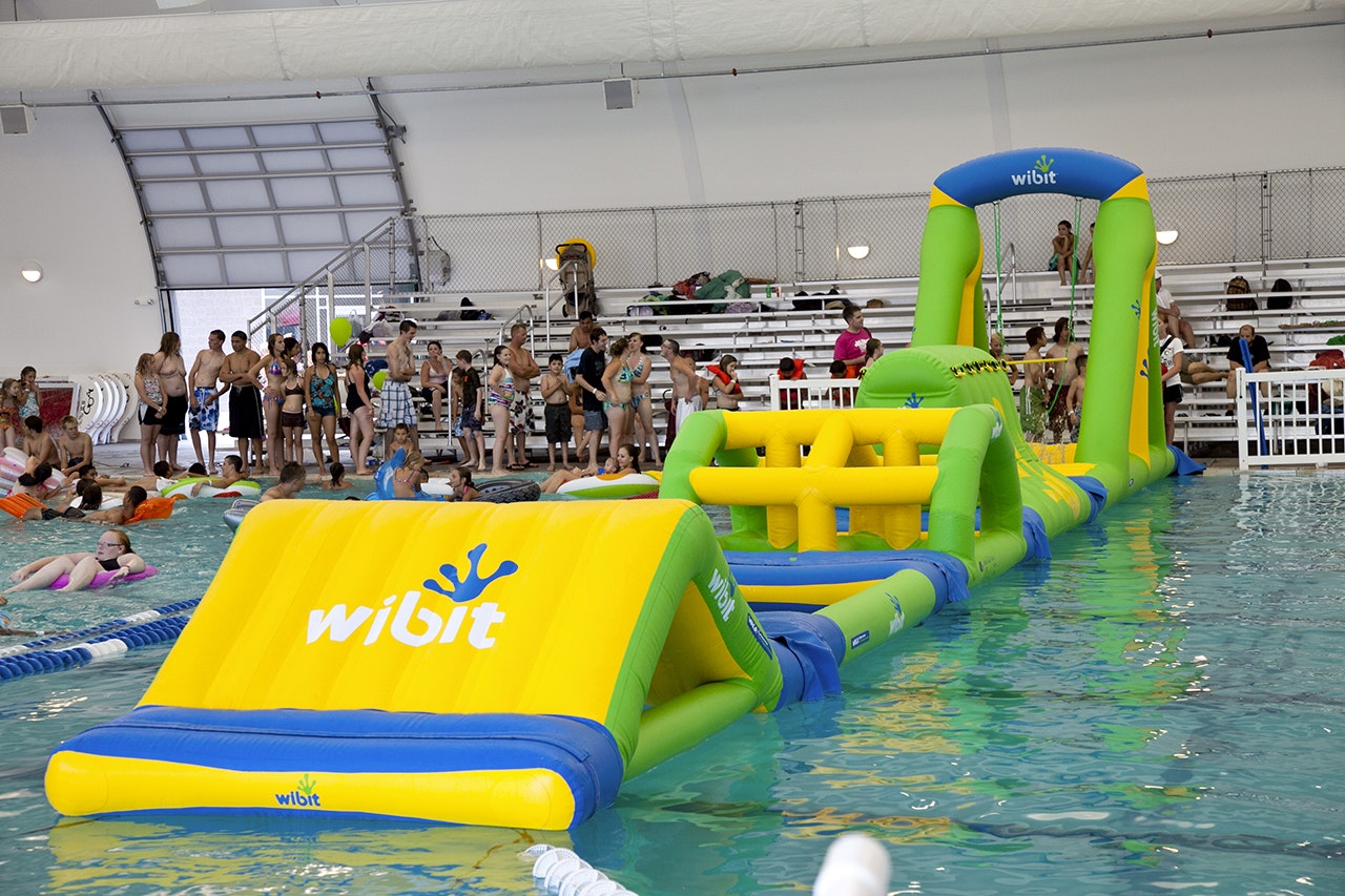 An indoor pool with an inflatable obstacle course and people swimming or waiting their turn.