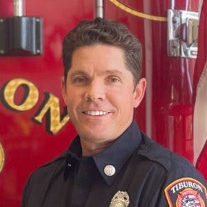 A firefighter is posing in uniform, with "Tiburon" visible on the uniform patch.