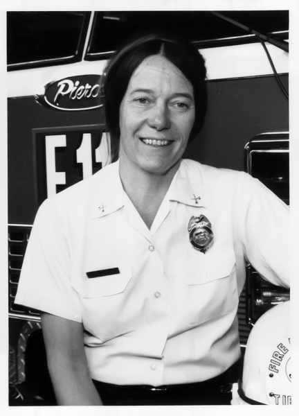 A person in a fire department uniform poses in front of a fire truck.