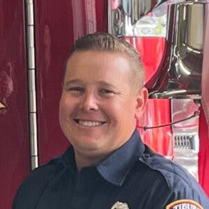 A person in a uniform smiling, standing in front of a fire truck.