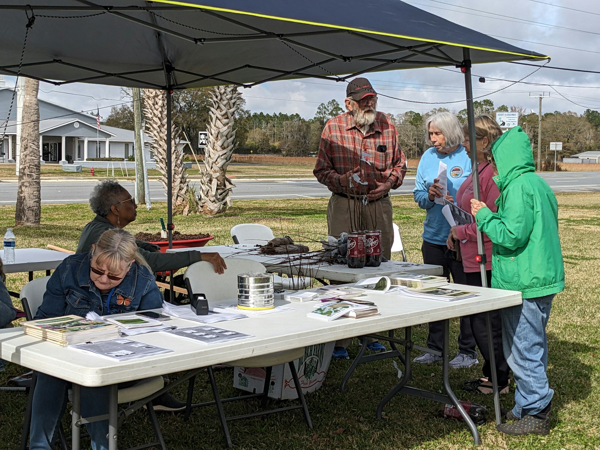 People gathered at a table with papers, under a canopy, possibly at a community event.