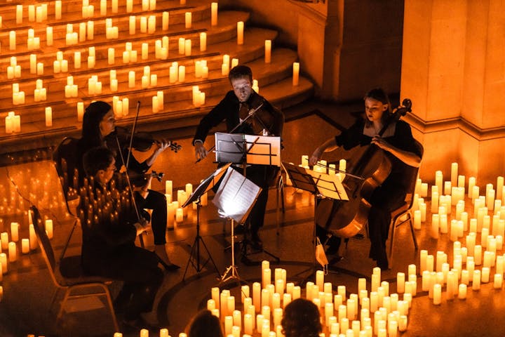 A string quartet performing surrounded by numerous lit candles in a dimly lit setting.