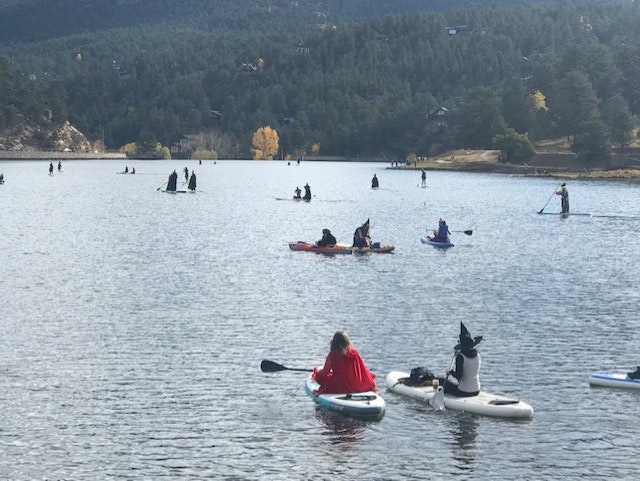 People in costumes are paddling on a lake surrounded by trees and hills.