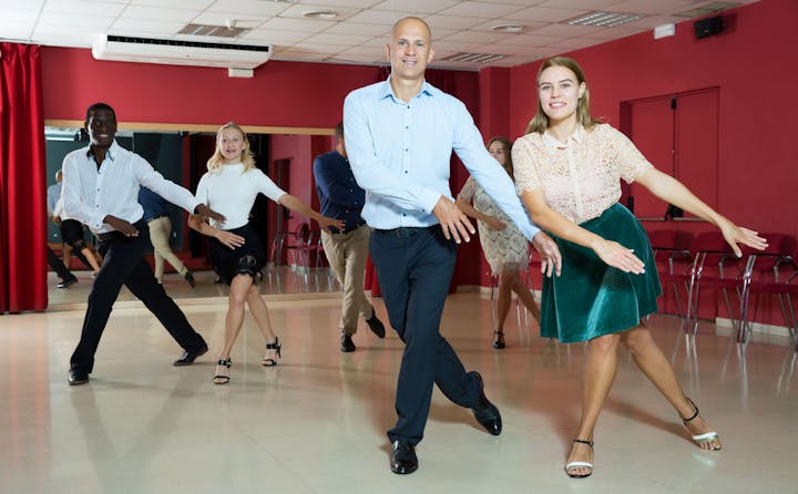 People dancing in a studio with mirrors and a red curtain.