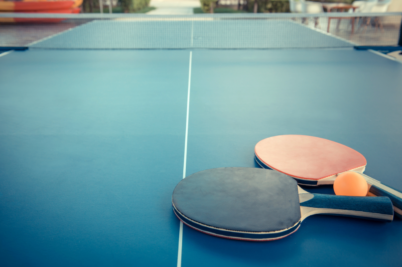 Two table tennis paddles (black and red) and an orange ball on a ping pong table.