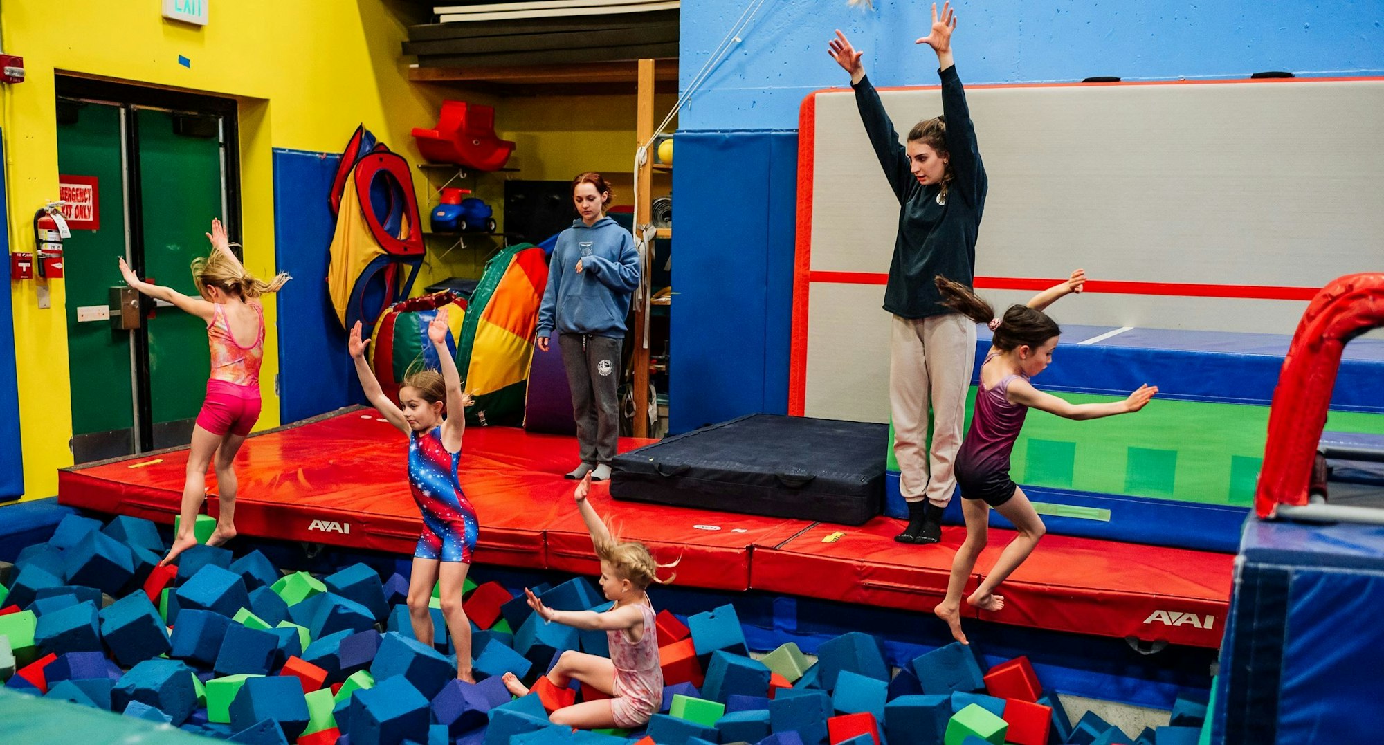 Children play in a colorful gym with foam blocks, mats, and gym equipment.