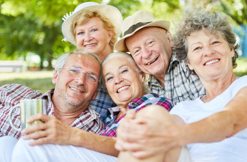 A happy group of five seniors enjoys a sunny day outdoors, smiling and posing together in a relaxed setting.