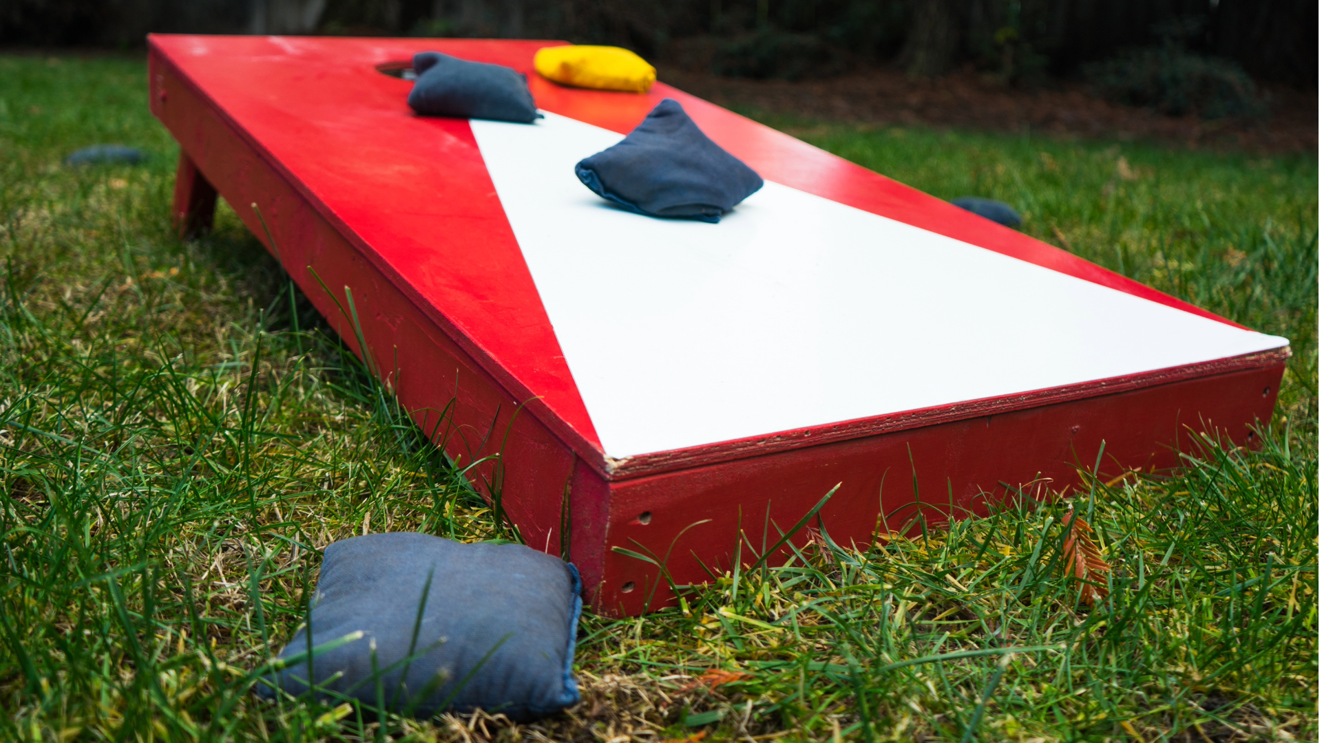 A red and white cornhole board with bean bags on a grassy lawn.