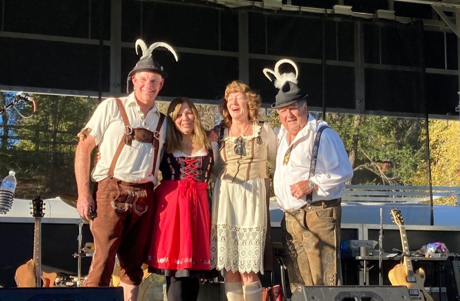 Four people in traditional Bavarian outfits on stage, smiling at the camera.