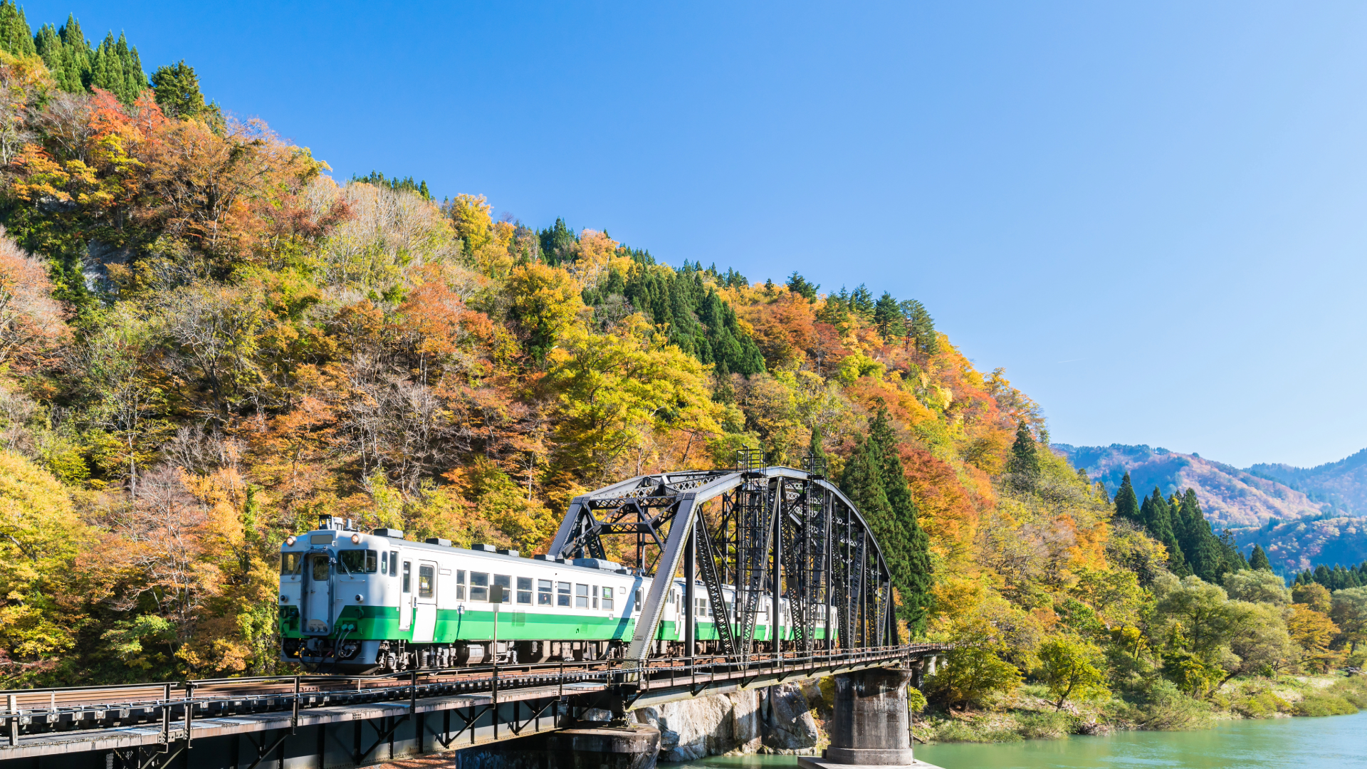 Train crossing a truss bridge with colorful autumn foliage.