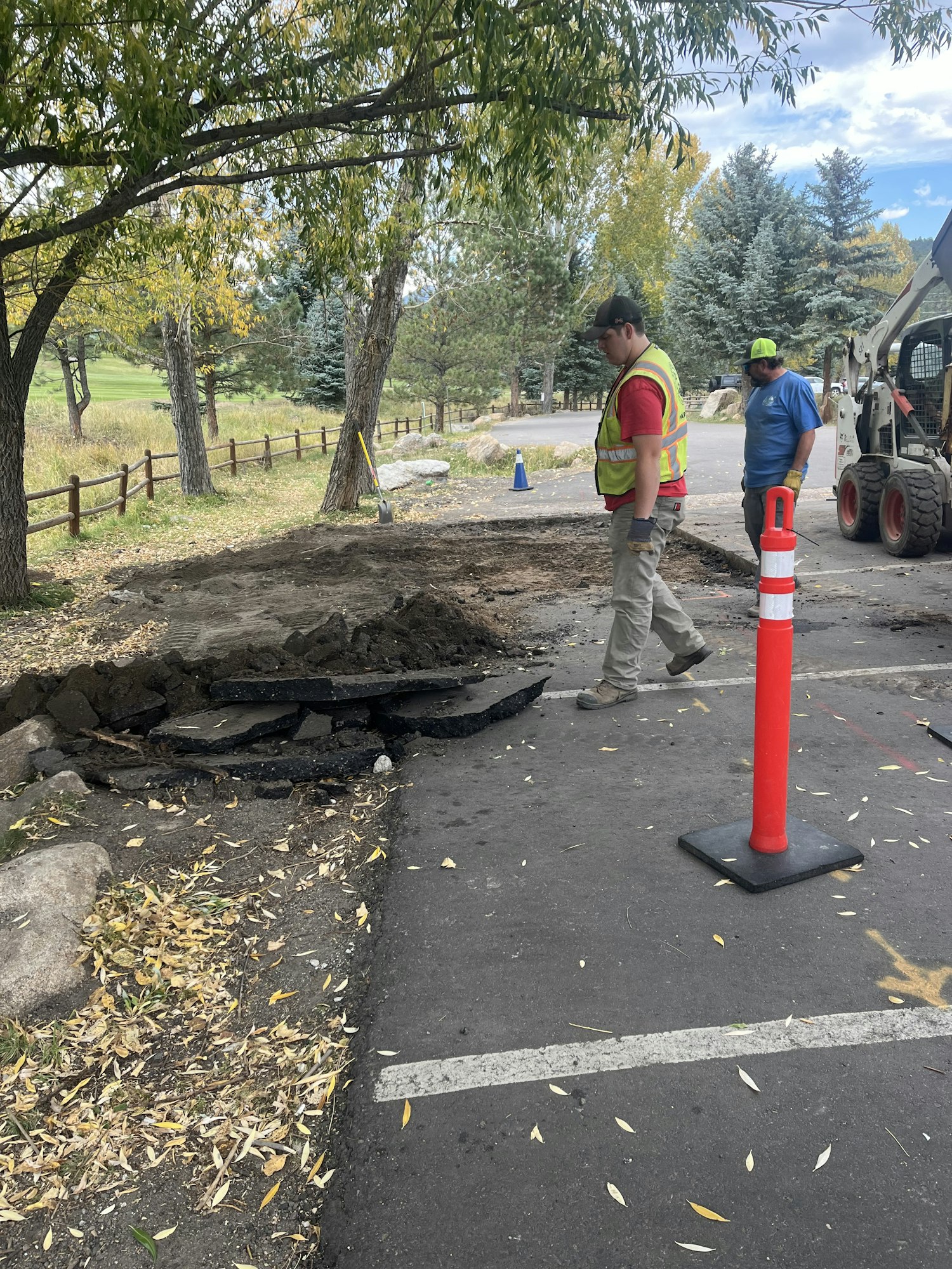 Construction workers repair a road section; equipment and traffic cones are visible.