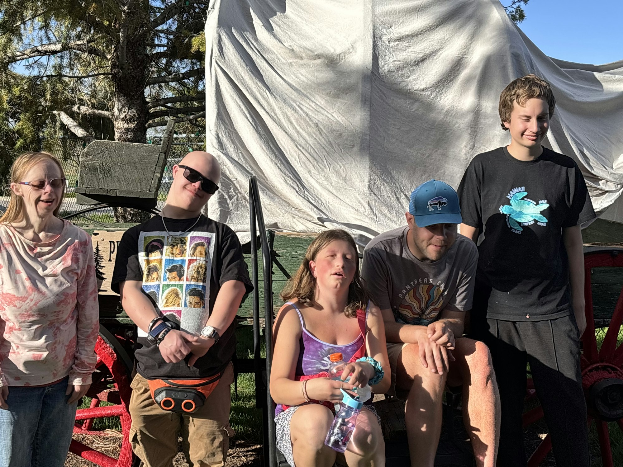 Five people posing outdoors near a covered wagon.