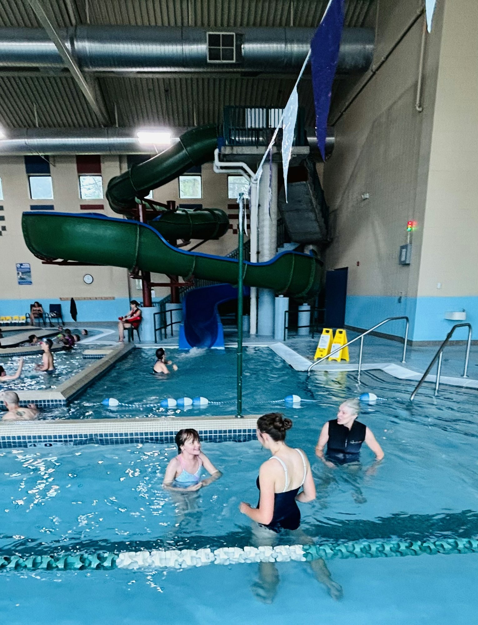 Indoor pool with slide, people swimming, and blue tiles.