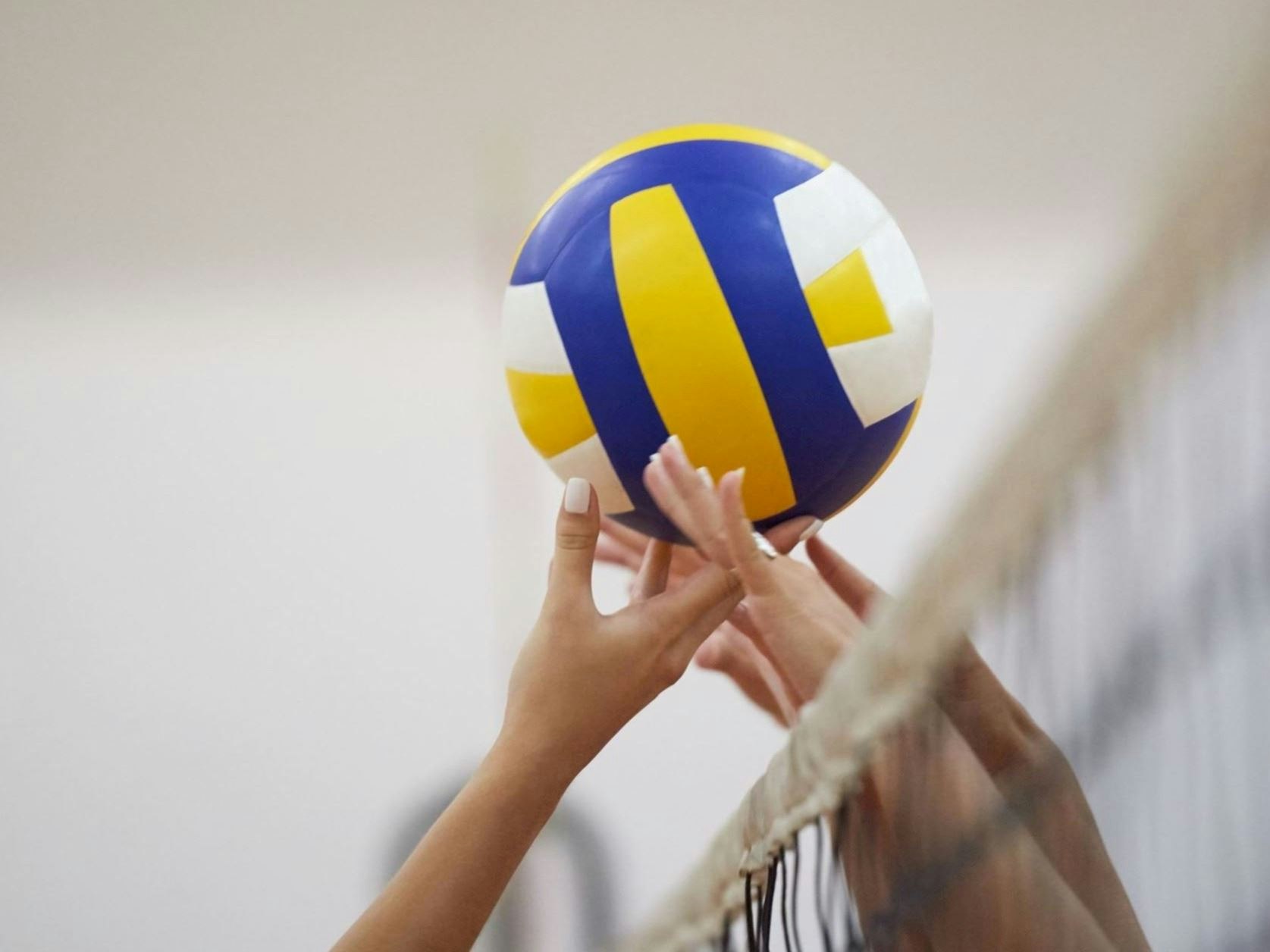 Hands reaching over a volleyball net, about to hit a colorful volleyball.