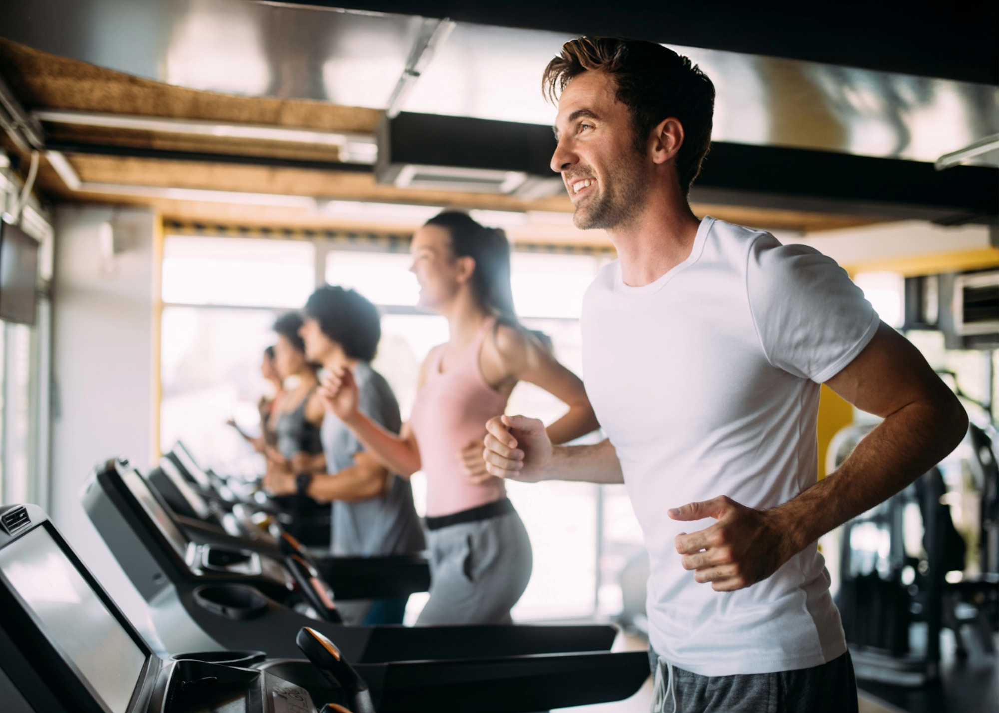 A group of people are jogging on treadmills in a gym, showcasing an energetic and healthy workout atmosphere.