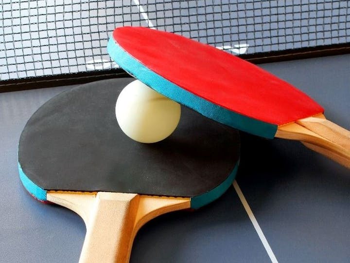 Two table tennis paddles and a ball on a table tennis table, with part of the net visible.