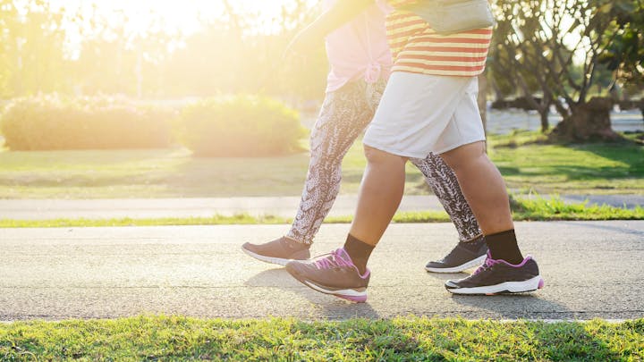 Two people walking on a path in a park, wearing athletic shoes with sunlight in the background.