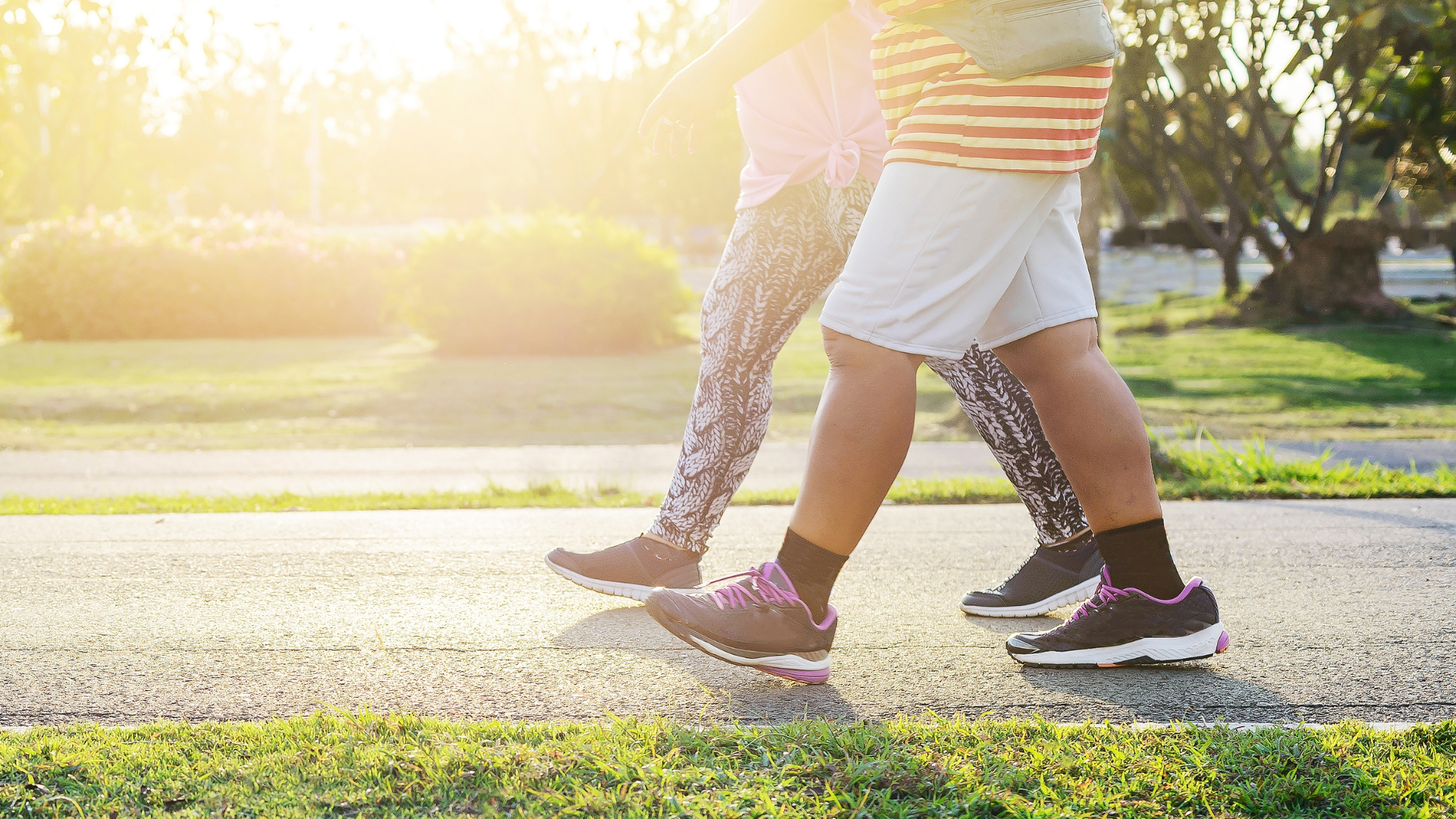 Two people walking on a path in a park, wearing athletic shoes with sunlight in the background.