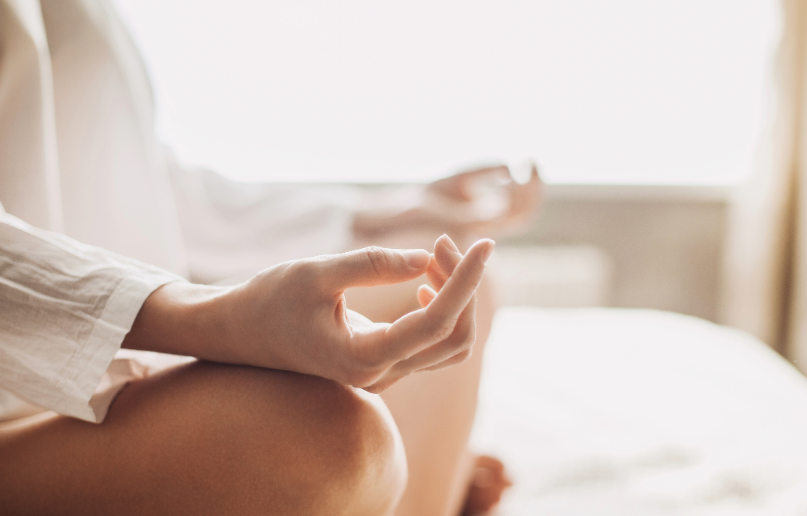 A person is sitting cross-legged in a meditation pose with hands on knees in a bright, calm setting.