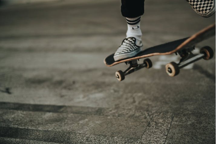 A person in checkered shoes is performing a skateboard trick on a concrete surface.