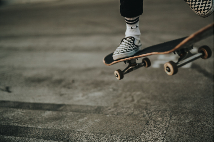 A person in checkered shoes is performing a skateboard trick on a concrete surface.