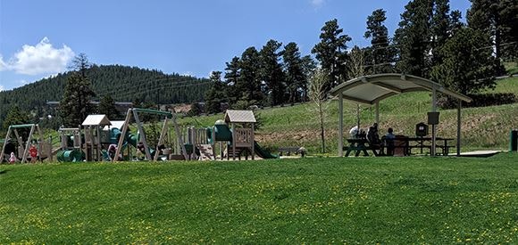 A playground with kids, a gazebo, picnic tables, and hillside in the background.