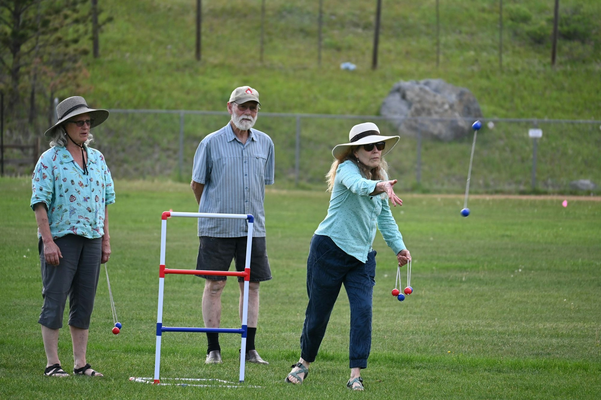 Three people playing a lawn game with a ball and target structure.