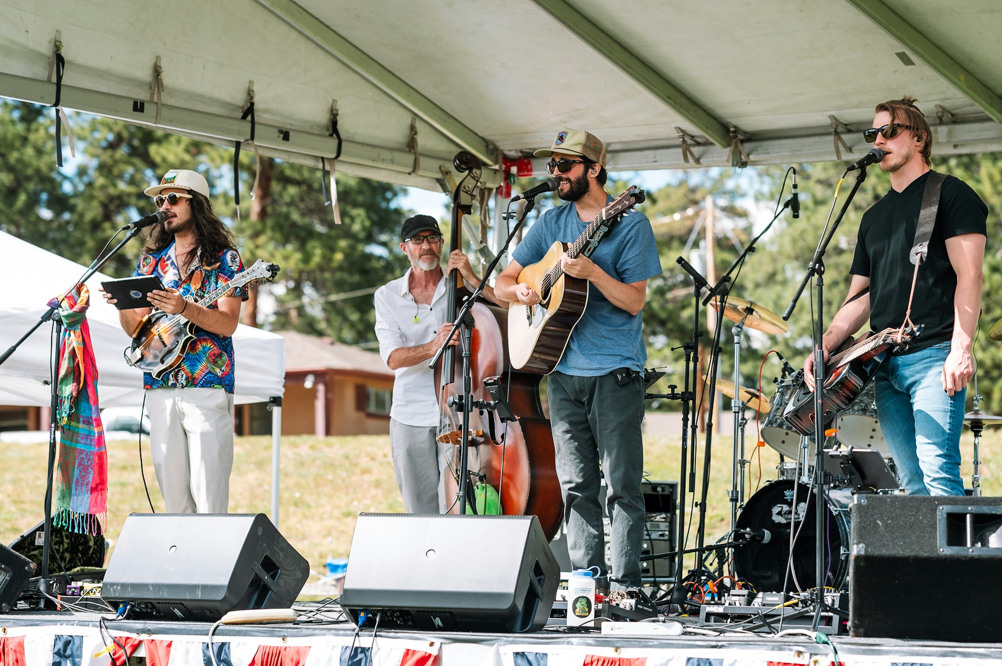 Four musicians performing on an outdoor stage with a variety of instruments.
