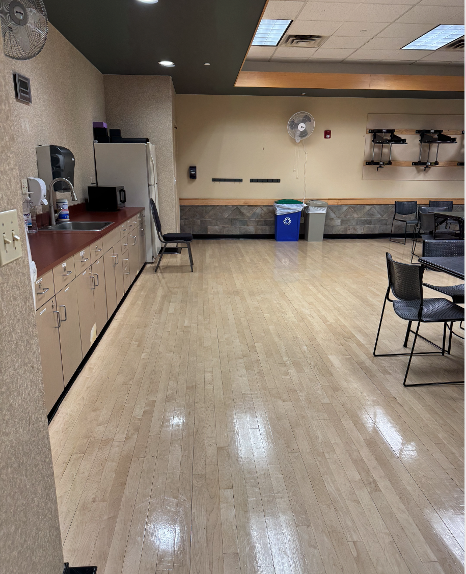 A break room with a kitchenette, tables, chairs, recycling bin, and fans on the wall.