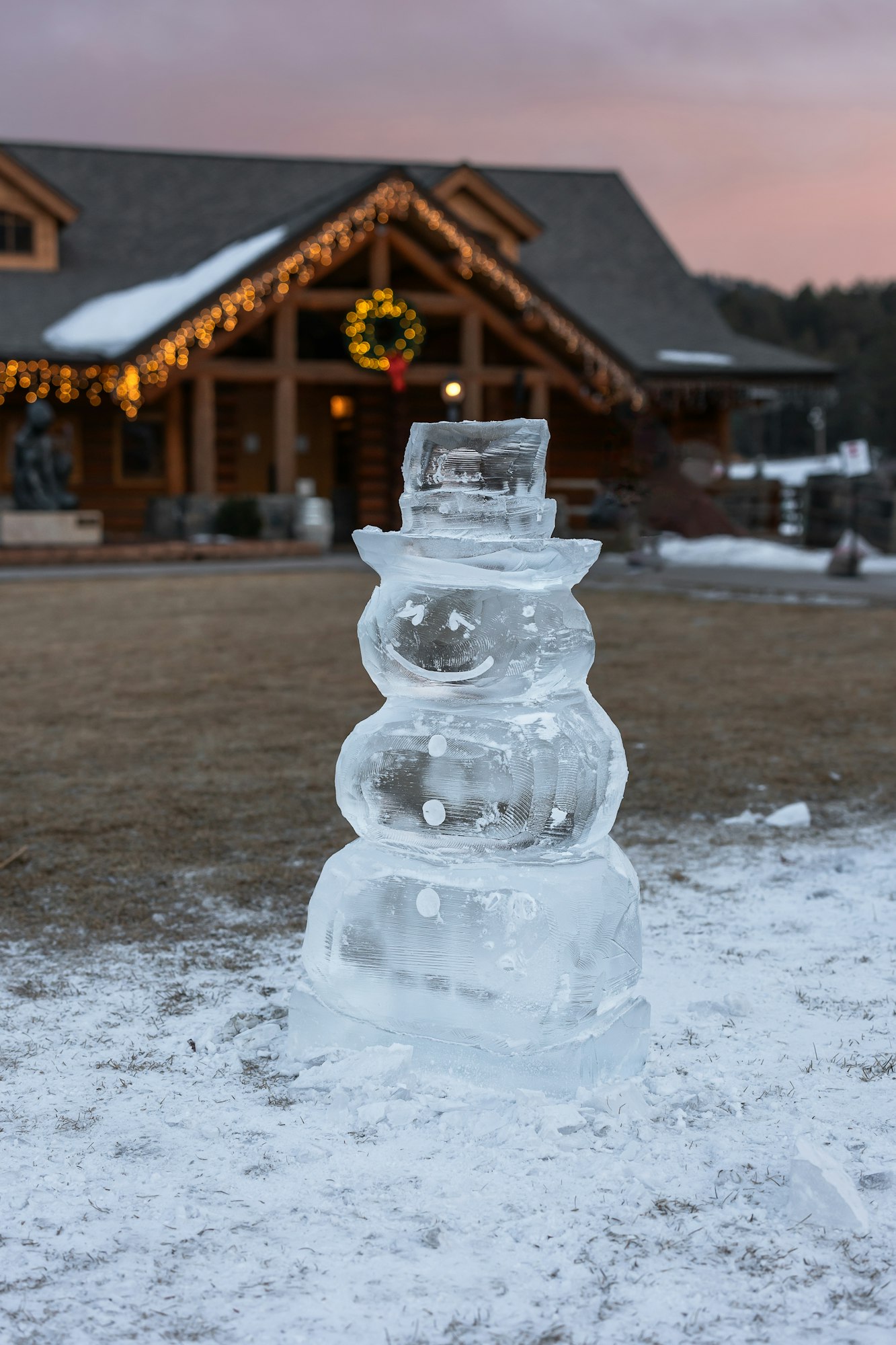 Ice sculpture of a snowman in front of a house decorated with lights and a wreath.