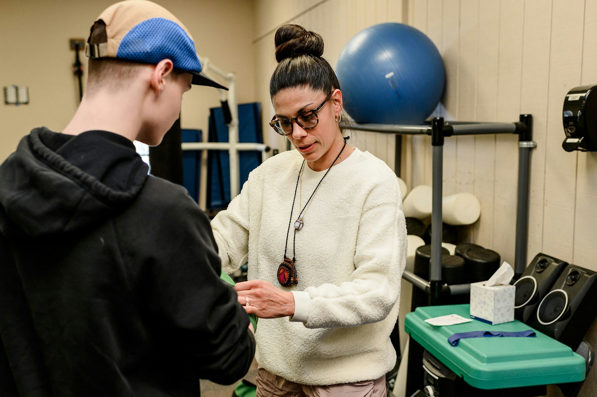 A woman and a young person in a gym, with the woman holding a tape measure, likely for a fitness assessment.