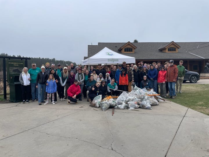 A large group of people posing with bags of collected trash at Evergreen Lake Trail, under a tent labeled "Evergreen."