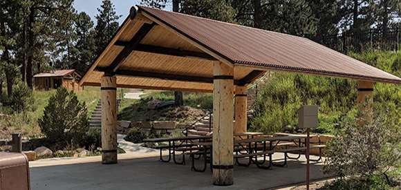 A sheltered picnic area with tables and a pathway leading through a park-like setting with trees.