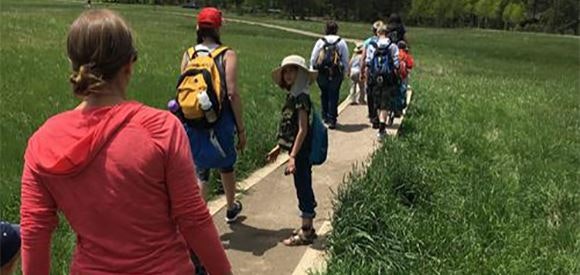A group of people hiking on a trail in a grassy area.