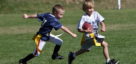 Two kids playing flag football, one running with the ball and the other trying to catch him.